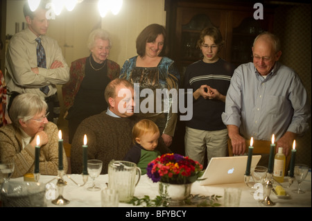 Famiglia riunita intorno al computer portatile a cena in famiglia Foto Stock