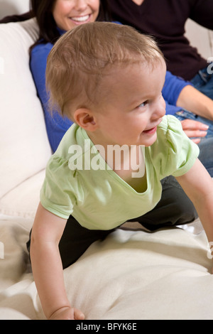 Baby boy strisciando sul divano con i suoi genitori in background Foto Stock