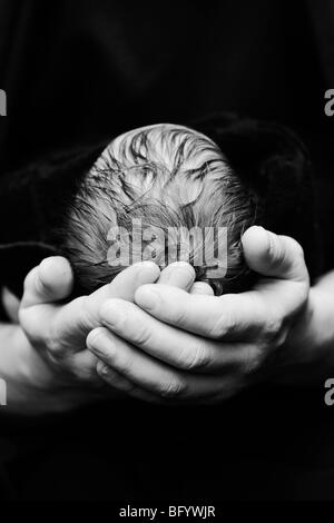 Una fotografia in bianco e nero di un neonato caucasico la testa del bambino di essere cullato nel suo padre le mani Foto Stock