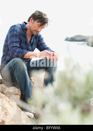 Uomo seduto sulla roccia a scogliere Foto Stock
