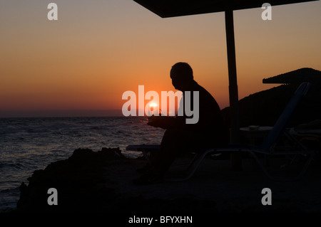 Zante. Zante. All'alba. Uomo in vacanza a guardare il tramonto sul mare dal promontorio tra Banana beach e Ag. Nikolaou (Agios Nikolaos) Foto Stock