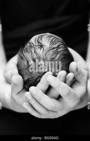 Una fotografia in bianco e nero di un neonato caucasico la testa del bambino di essere cullato nel suo padre le mani Foto Stock