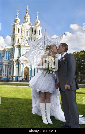 Amare la coppia appena sposata baciare. Rimanendo sulla erba verde nei pressi della chiesa sotto il cielo blu Foto Stock