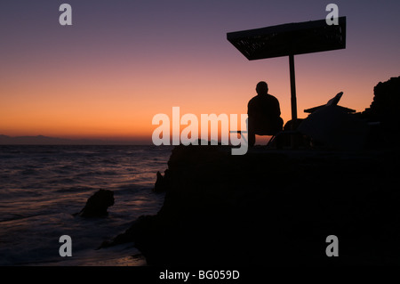 Zante. Zante. All'alba. Uomo in vacanza a guardare il tramonto sul mare dal promontorio tra Banana beach e Ag. Nikolaou (Agios Nikolaos) Foto Stock