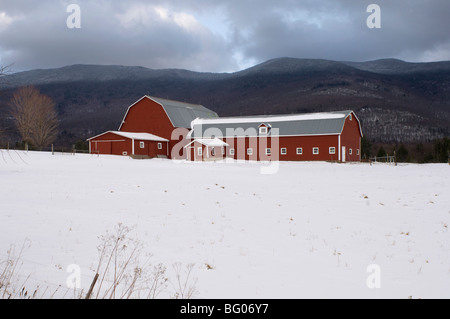 Un tradizionale dipinto di rosso fienile circondato da neve e il verde delle montagne sullo sfondo, Vermont, New England, STATI UNITI D'AMERICA Foto Stock