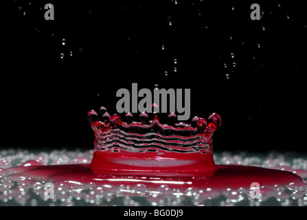 Una goccia di rosso acqua formando un coronet come esso cade in uno strato superficiale di liquido Foto Stock