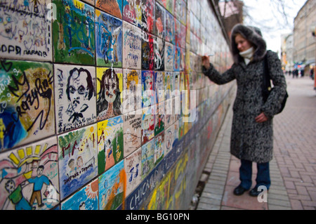 Una giovane donna scrive il suo nome su graffiti ricoperti di piastrelle in Arbat Ulitsa, Arbatskaya, Mosca, Russia, Europa Foto Stock