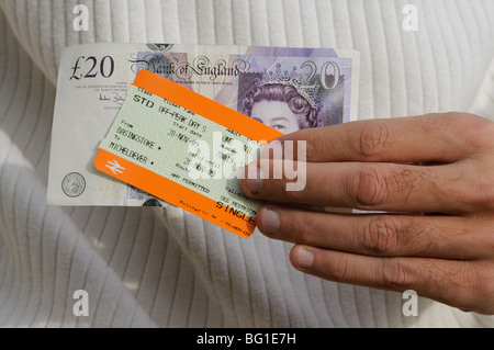 Biglietto ferroviario e venti pound nota che viene tenuto in una mano mans Foto Stock