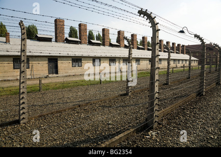 Perimetro recinto elettrico ad Auschwitz nazista di morte nel campo di Oswiecim, Polonia. Camini dal blocco cucina sono visibili dietro. Foto Stock