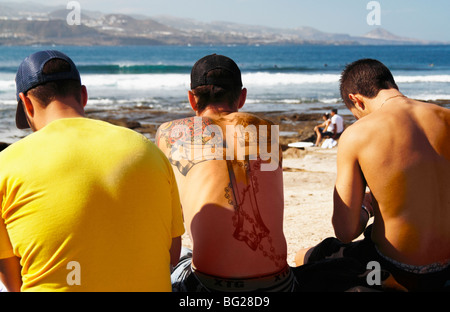 Uomo con croce tatooed sul retro guarda la gara di surf in Spagna Foto Stock