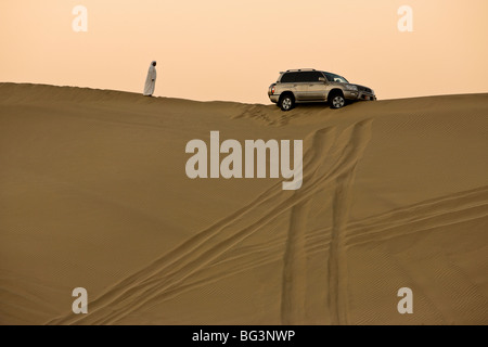 Uomo in abito arabo guardando 4x4 vettura bloccato sul crinale di una duna durante un safari nel deserto vicino a Abu Dhabi, Emirati Arabi Uniti Foto Stock