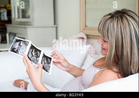 Donna incinta seduta sul divano con baby scan Foto Stock