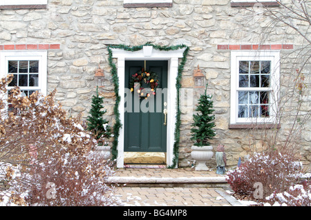 Un bel colpo di una vendemmia storica casa in pietra decorato per il Natale. Una corona di un verde porta anteriore sempreverdi e la ghirlanda. Foto Stock