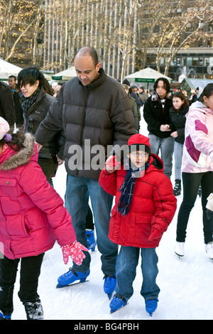 Little Girl lost in wonder aggrappandosi saldamente al papà in mano come si struttura di pattino nella folla multiculturale sul pattinaggio stagno in Bryant Park New York Foto Stock