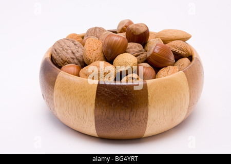 Ciotola di legno riempita con dadi misti nei loro gusci di nocciole, noci e mandorle. Foto Stock