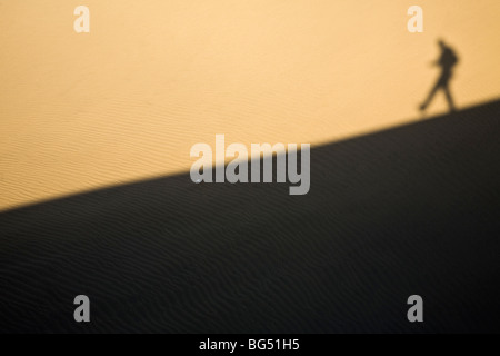 Ombra di un uomo che cammina verso il basso di una duna di sabbia Foto Stock