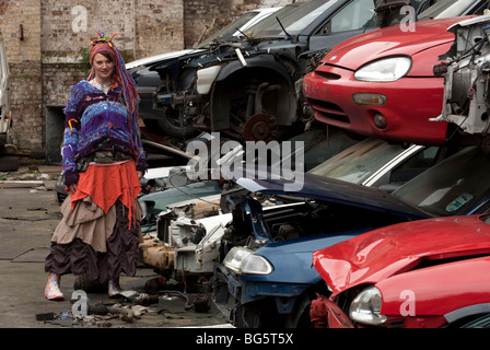 Modello femminile in auto nel cortile di scarto con luminosi abiti colorati e i capelli. Modello completamente rilasciato Foto Stock