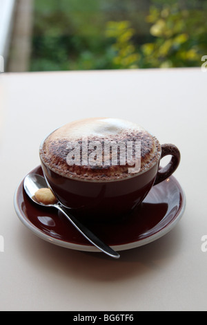 Cappuccino con una croce di cioccolato sulla parte superiore in una tazza di colore blu e il piattino su un tavolo blu Foto Stock