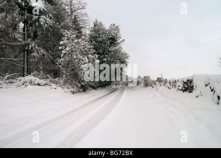 Una piccola strada con la foresta nella campagna inglese di Hampshire dopo una nevicata con tracce di pneumatici nella neve Foto Stock