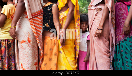 Staring ragazza indiana in piedi tra le madri indossa sari colorati in una coda. Andhra Pradesh, India Foto Stock