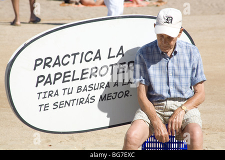 VECCHIO, ANZIANO, SPIAGGIA, BARCELLONA: Un vecchio si siede di fronte a un cartello informativo pubblico al sole sulla spiaggia di Barcellona in Spagna Foto Stock