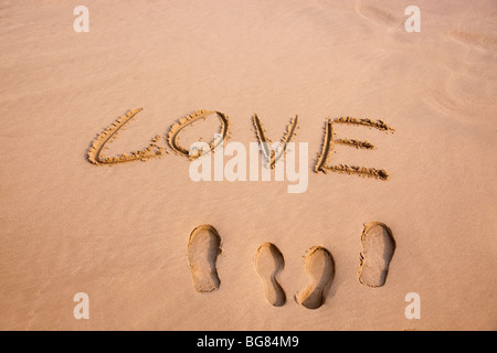 Due coppie di footprint e amore scritto di sabbia su una spiaggia Foto Stock