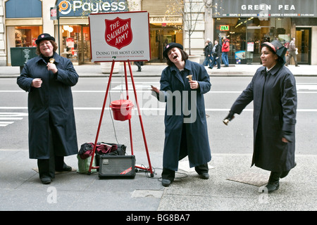 Delizioso Esercito della Salvezza bell ringer sciorinando labbro sincronizzate canti di Natale nella speranza di riempire i loro bollitore sulla Quinta Avenue Foto Stock
