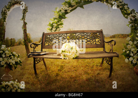 In legno molto bello e banco di ferro all'aperto su un ampio campo di fiori decorato arch dietro e una sposa bouquet su Foto Stock