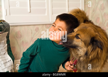 6-7 anni ragazzo ispanico essendo lambito sulla guancia con il suo mix di chow cane leccare la faccia signor vista laterale frontale © Myrleen Pearson Foto Stock