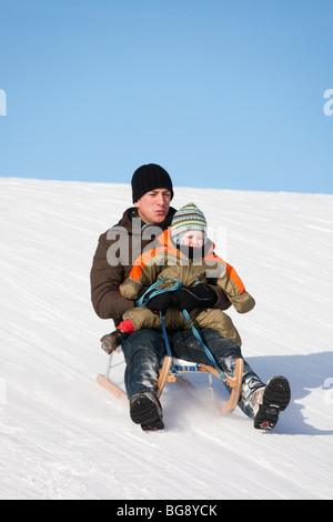 Uomo con un bambino piccolo sul suo ginocchio toboga in discesa su un pendio di neve. Austria Europa. Foto Stock