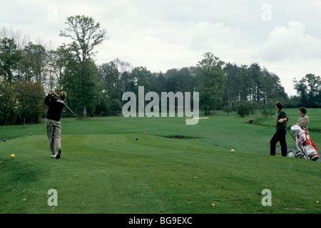 Giocatore di golf tees off su di un campo da golf mentre due giocatori watch Foto Stock