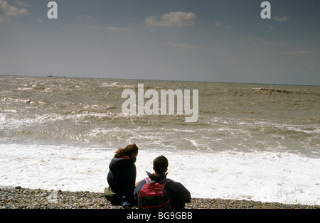 Due escursionisti seduto sulla spiaggia guardando le onde che si infrangono Foto Stock