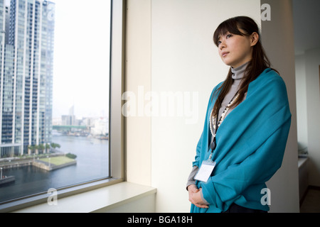 Giovane donna in piedi dalla finestra Foto Stock