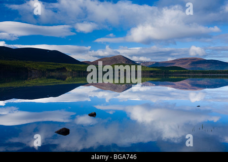 La Scozia, altopiani, Cairngorms National Park. Nuvole, la foresta e la montagna si riflette sulle acque tranquille del Loch Morlich Foto Stock