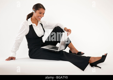 Giovane donna seduta sul pavimento con il laptop e indossando auricolare blue tooth. Formato orizzontale. Foto Stock