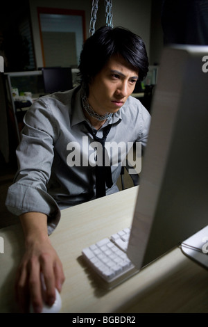 Giovane Uomo in camicia e cravatta è appeso da una catena a sua cabina mentre si utilizza il computer Foto Stock