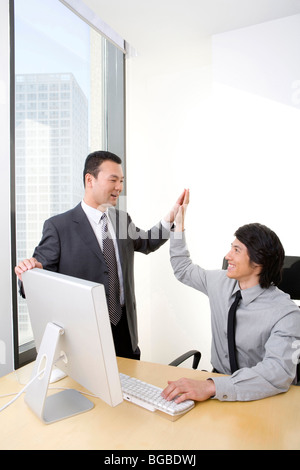 Uomo in tuta di business ad alta cinque giovani dipendente che sta utilizzando un computer Foto Stock
