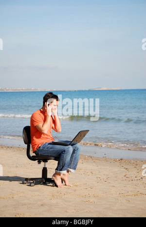 Giovane uomo con il computer portatile sulla spiaggia Foto Stock