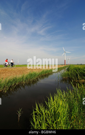 I ciclisti nella parte anteriore delle turbine eoliche, Sexbierum, Friesland, Holland, Paesi Bassi, Europa Foto Stock