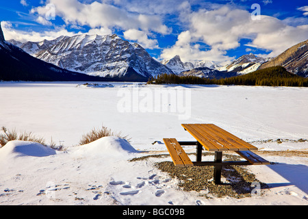 Tavolo da picnic sulle rive di un congelato e coperta di neve in alto lago Kananaskis durante l'inverno, backdropped dalla gamma di Kananaskis Foto Stock