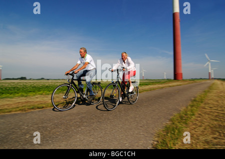 I ciclisti nella parte anteriore delle turbine eoliche, Sexbierum, Friesland, Holland, Paesi Bassi, Europa Foto Stock