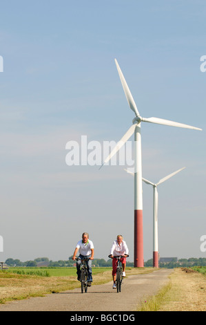 I ciclisti nella parte anteriore delle turbine eoliche, Sexbierum, Friesland, Holland, Paesi Bassi, Europa Foto Stock