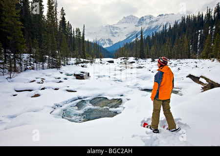 Una donna che indossa scarpe da neve guardando la coperta di neve in inverno il paesaggio circostante il fiume Mistaya con montatura Sarbach (3155 m Foto Stock