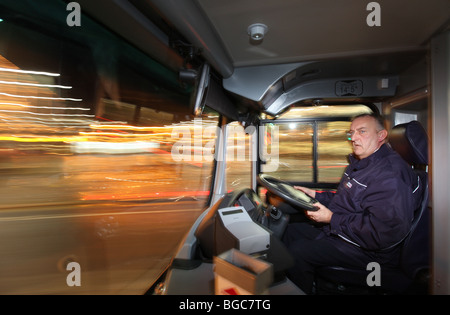 Autista di autobus nel Regno Unito alla guida del suo servizio pubblico di bus del veicolo durante la notte in una città Foto Stock