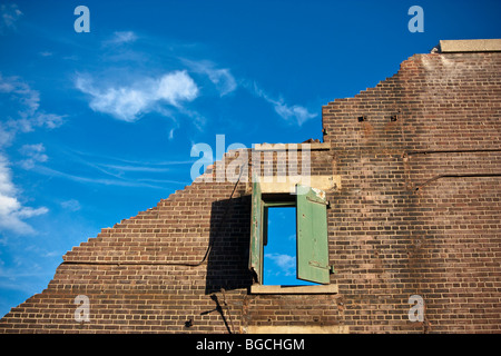 Inquadratura concettuale di un edificio demolito. Parete singola rimane con una finestra in essa, il cielo blu e nuvole bianche. Foto Stock