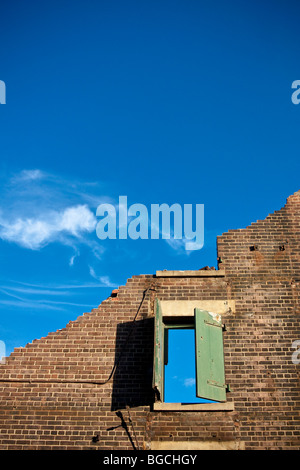 Inquadratura concettuale di un edificio demolito. Parete singola rimane con una finestra in essa, il cielo blu e nuvole bianche. Foto Stock