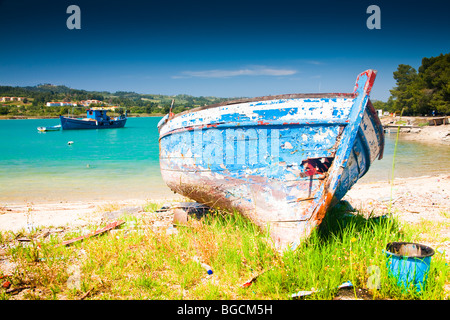 Una barca a remi in legno barca da pesca si trova tirato fino alla riva. È di colore rosso e bianco di vernice blu che si staccava e il suo aspetto trascurato. Foto Stock