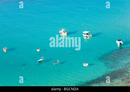 Piccola, luminosa giacciono barche ormeggiate in una baia poco profonda su un azzurro-mare colorati. Colpo da ombre di cui sopra può essere visto sul fondale. Foto Stock