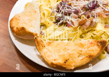 Piatto di tagliatelle si lancia in un pesto e olio di oliva con pancetta affumicata e cipolla rossa. Conditi con formaggio parmigiano grattugiato Foto Stock