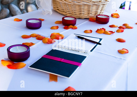 Wedding guest book con firme su una tabella con petali di fiori e candele votive Foto Stock